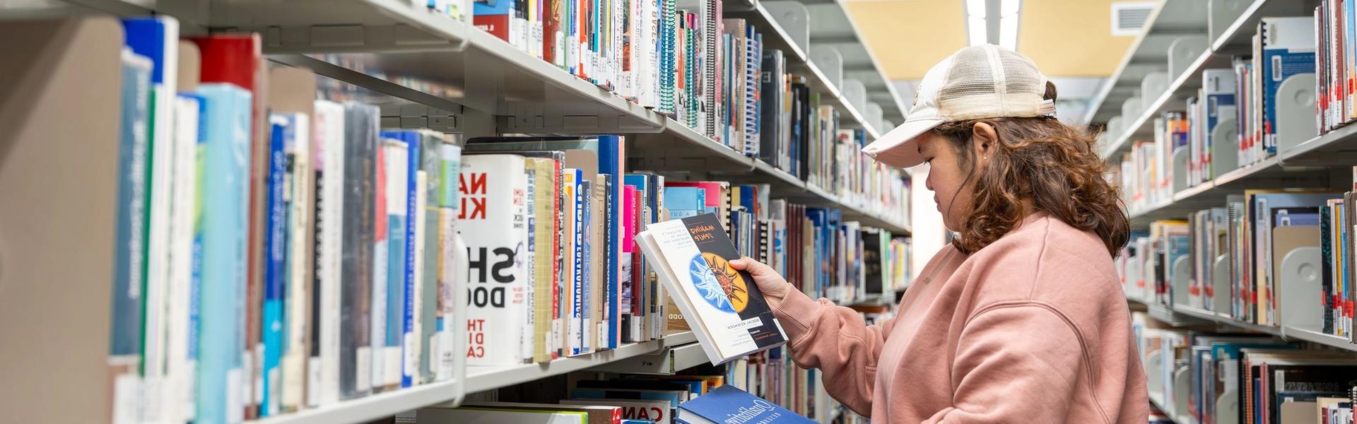 Student browsing library shelves and selecting books for study