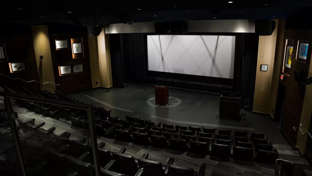 Empty campus theatre with large screen, podium, and tiered seating