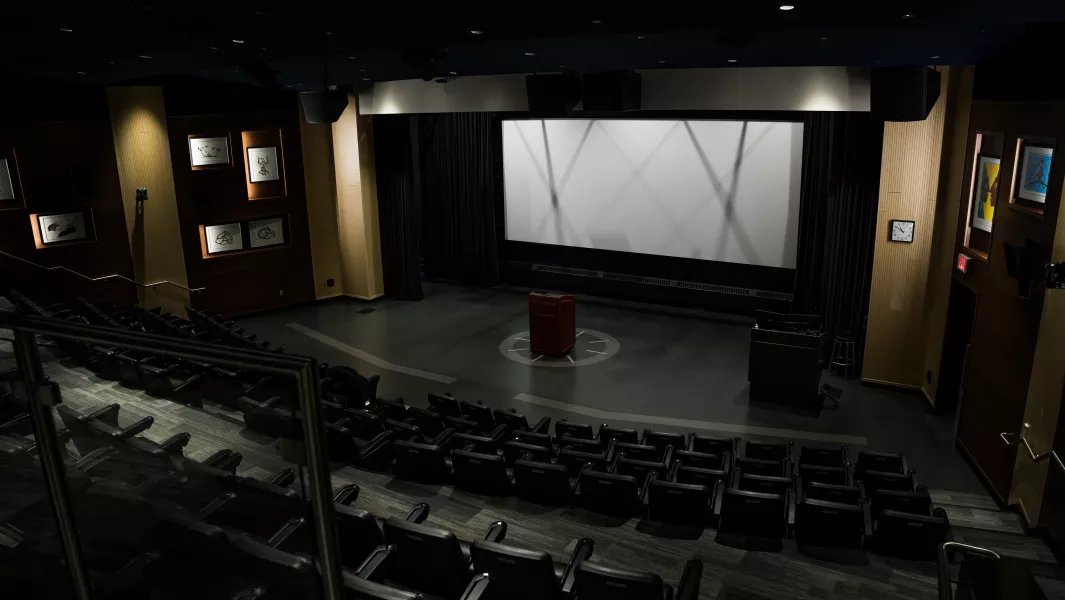 Empty campus theatre with large screen, podium, and tiered seating
