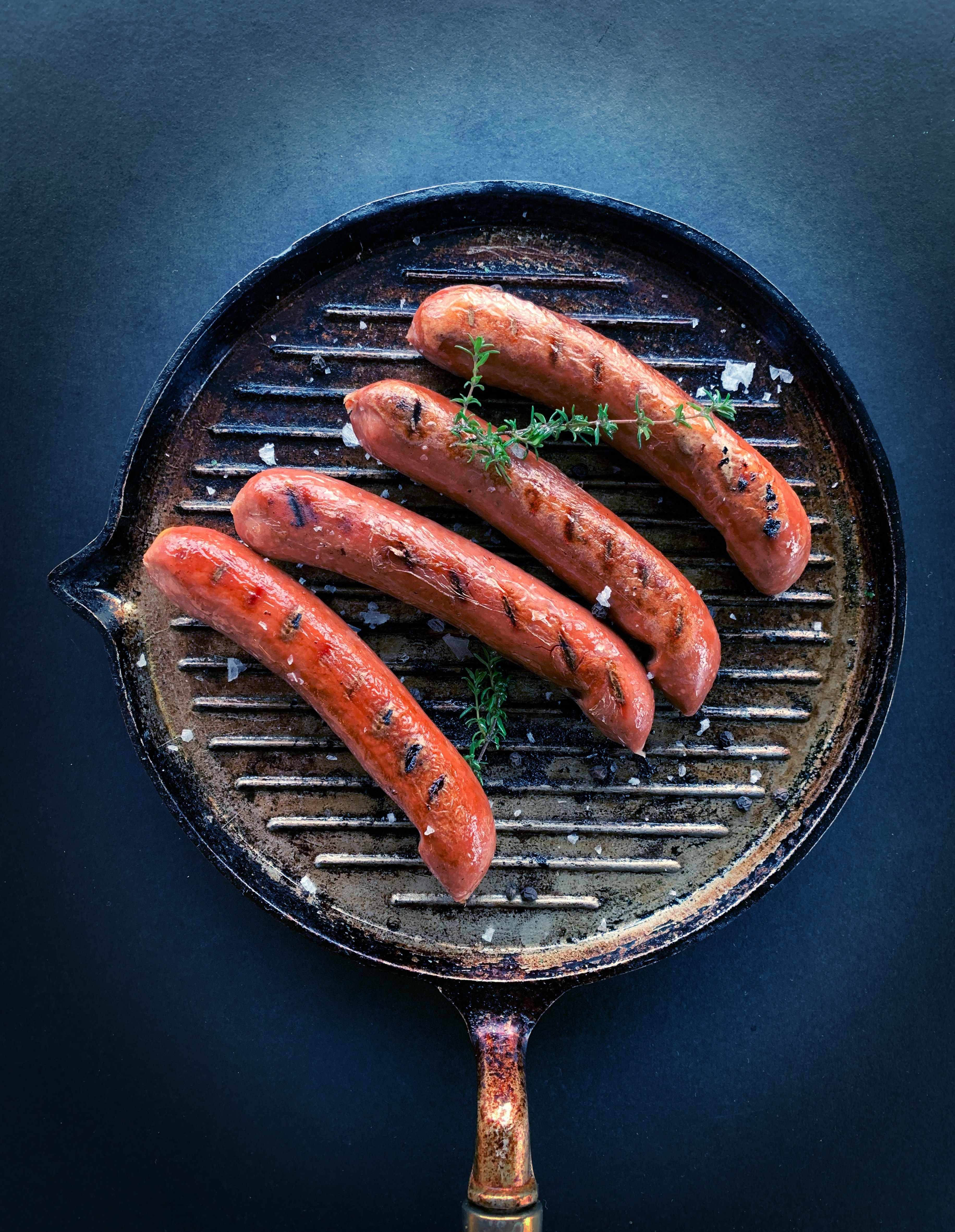 Four grilled sausages in a ridged skillet with sprigs of thyme