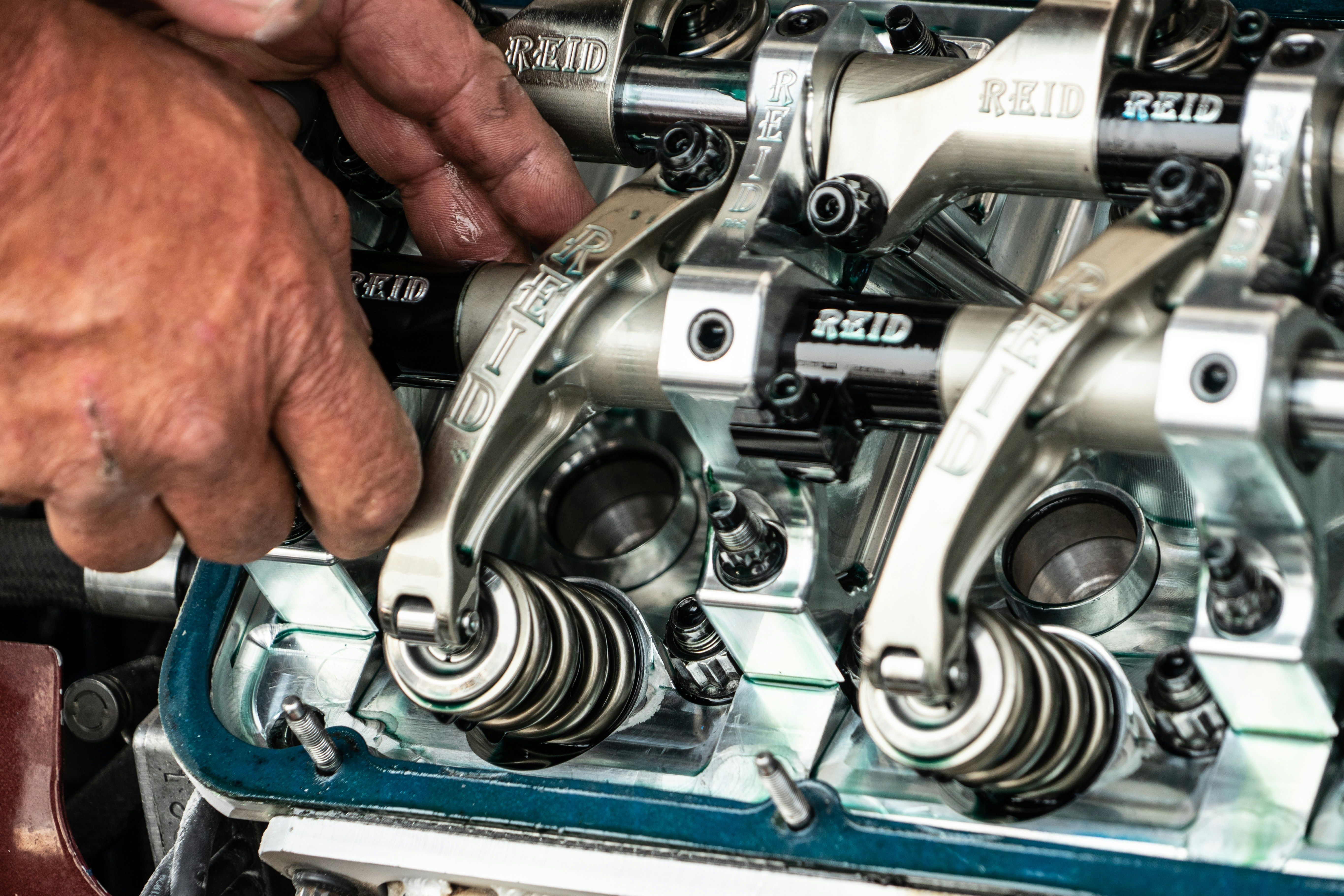 Hands adjusting shiny metal engine rocker arms and valve springs inside an engine head