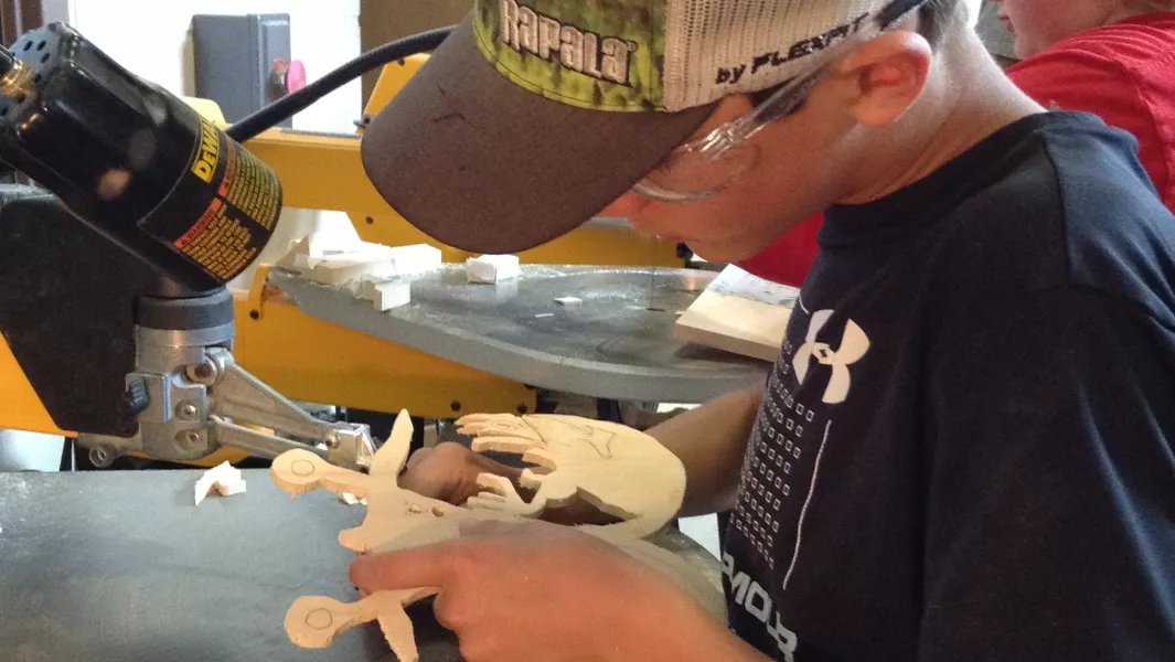 Student carefully cutting a wooden design with a scroll saw during summer camp