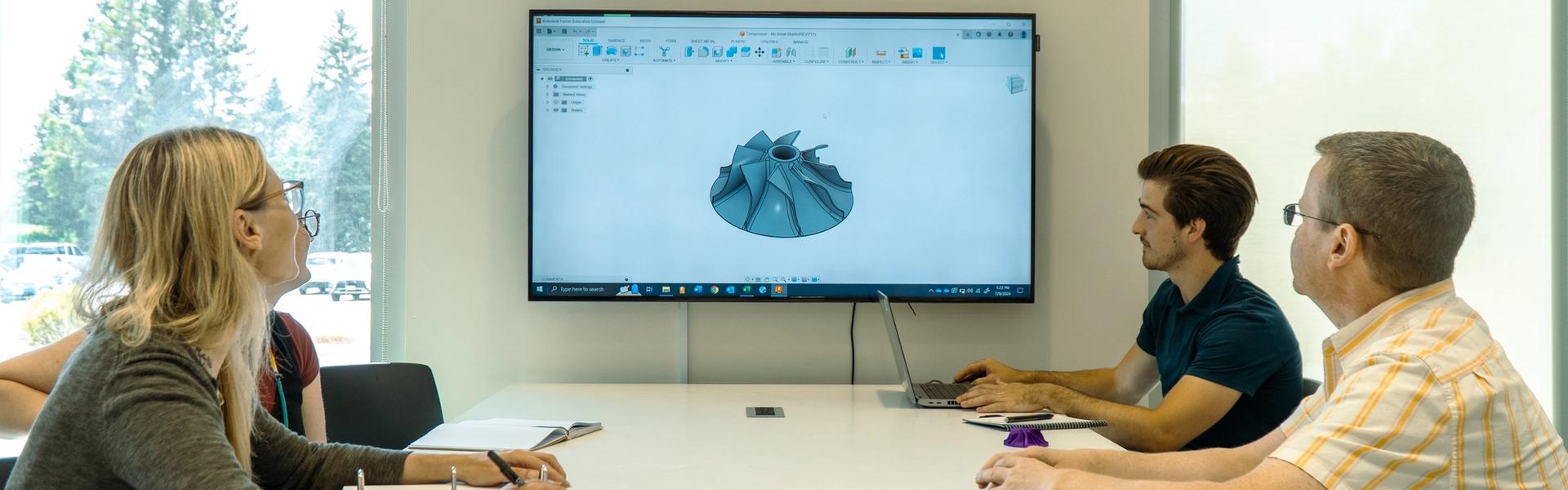Three people reviewing a 3D CAD model on a screen during a design meeting