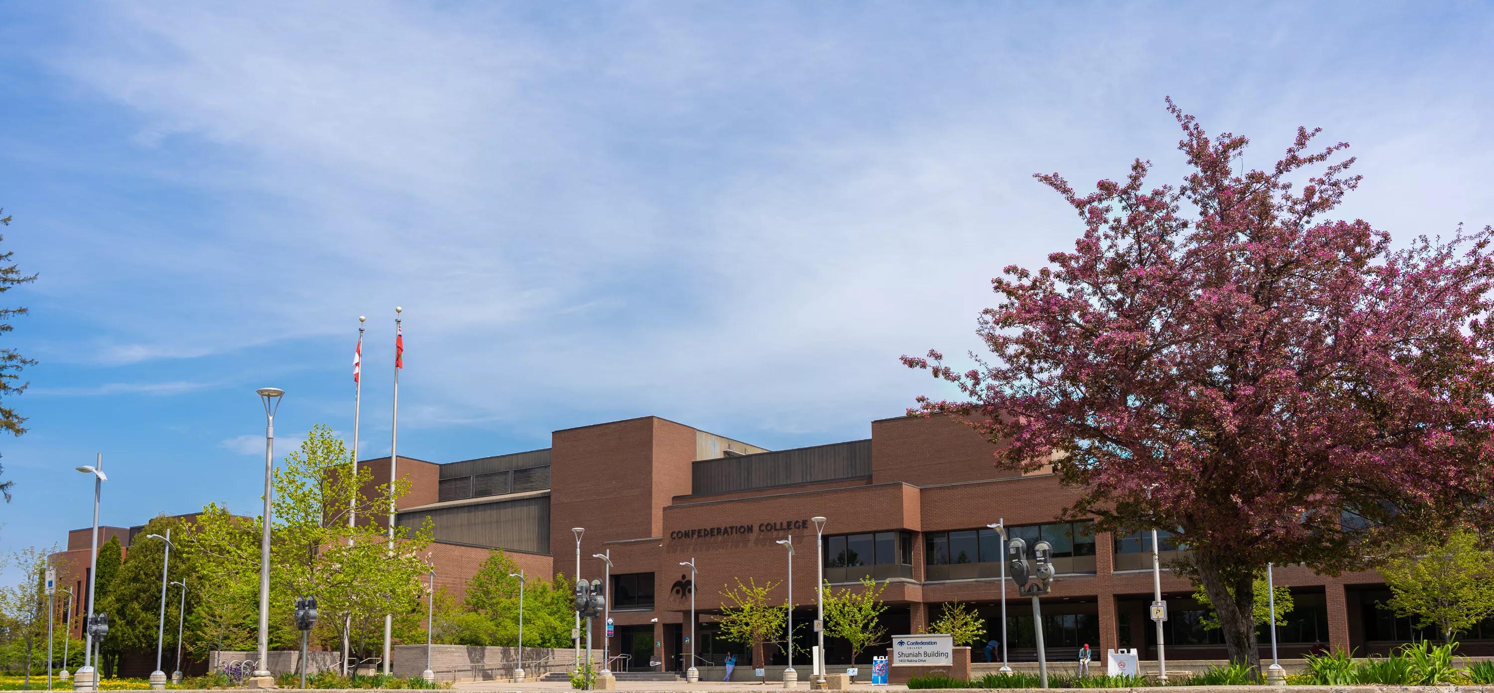Confederation College Shuniah Building exterior with flags and spring foliage