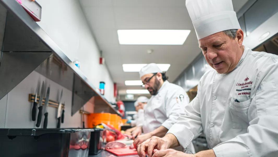 Chef instructor guiding students while preparing food in the kitchen
