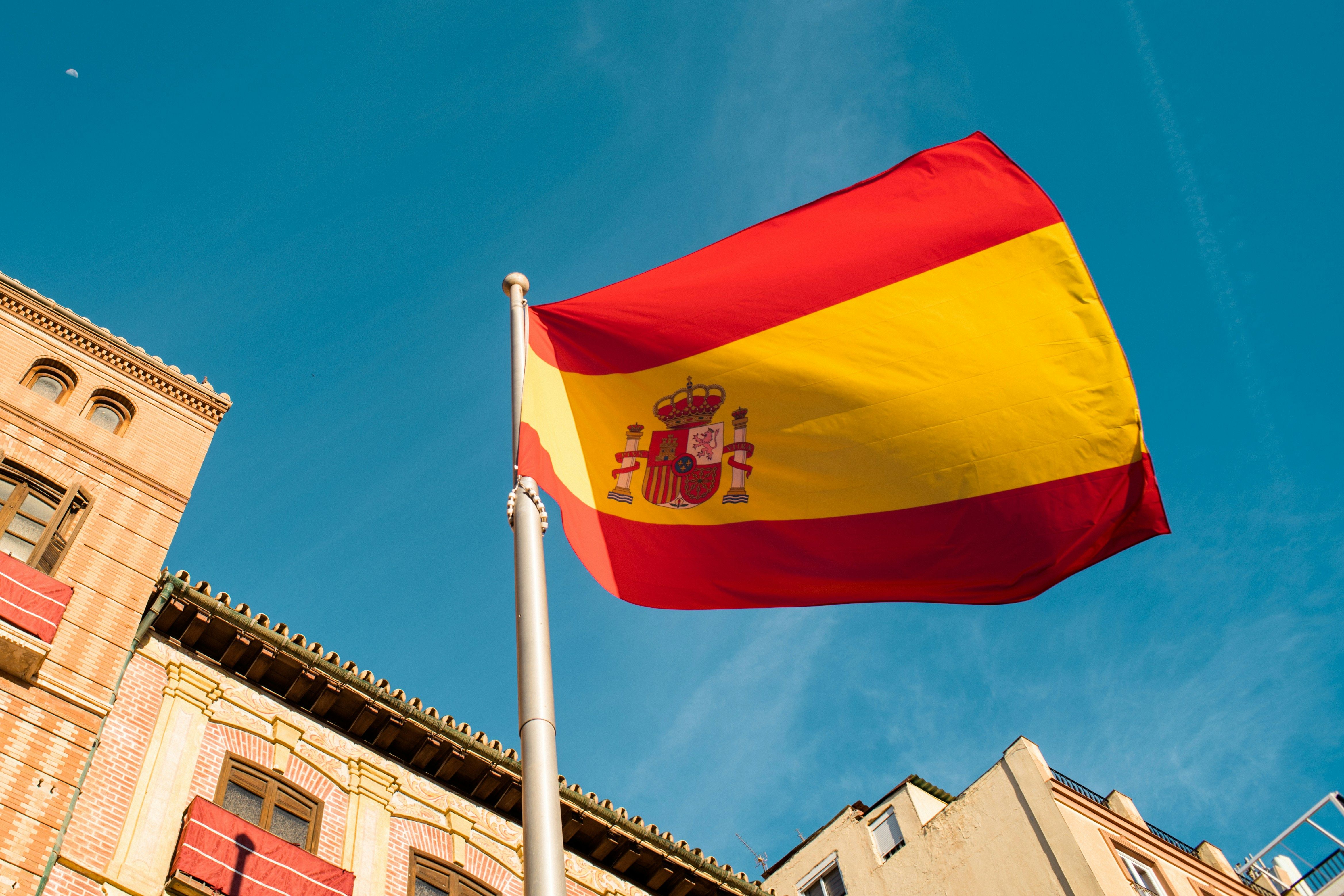 Spanish flag flying above low buildings against a blue sky