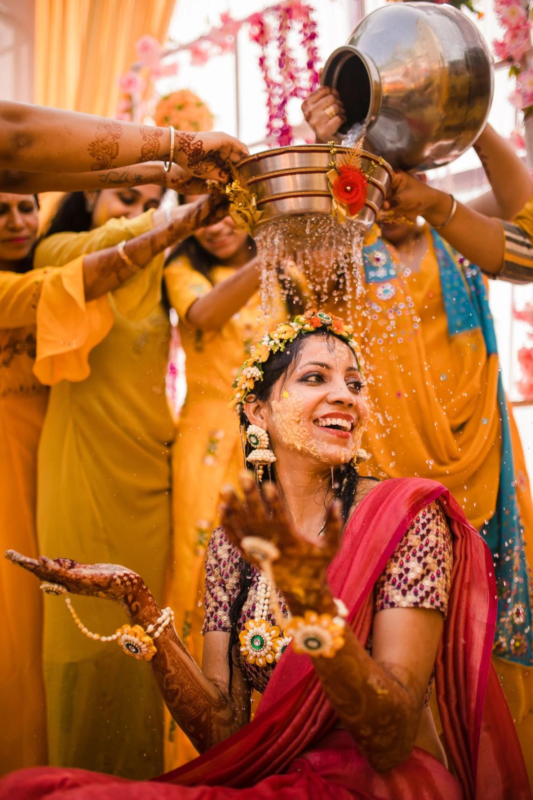 Bride laughing as haldi water is poured over her