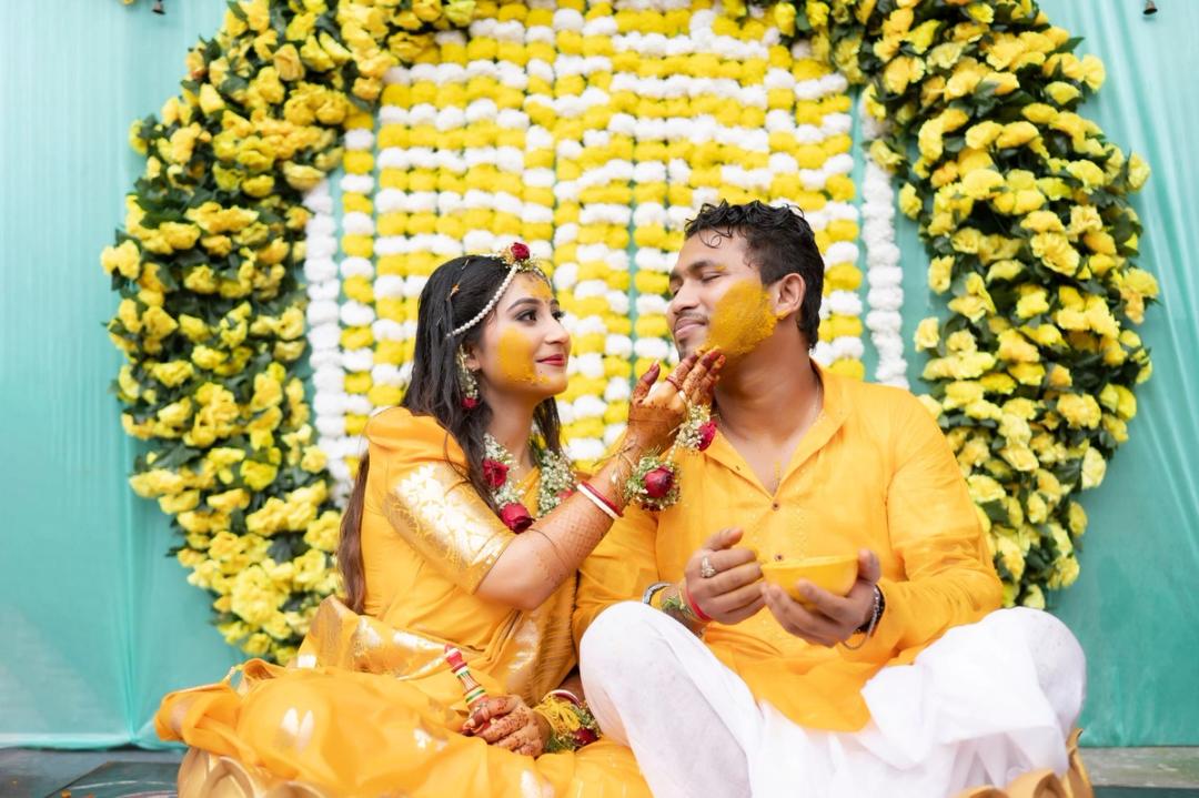 Couple feeding each other at their haldi, marigolds behind