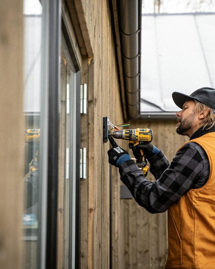 Elettricista al lavoro con il trapano su una parete in legno