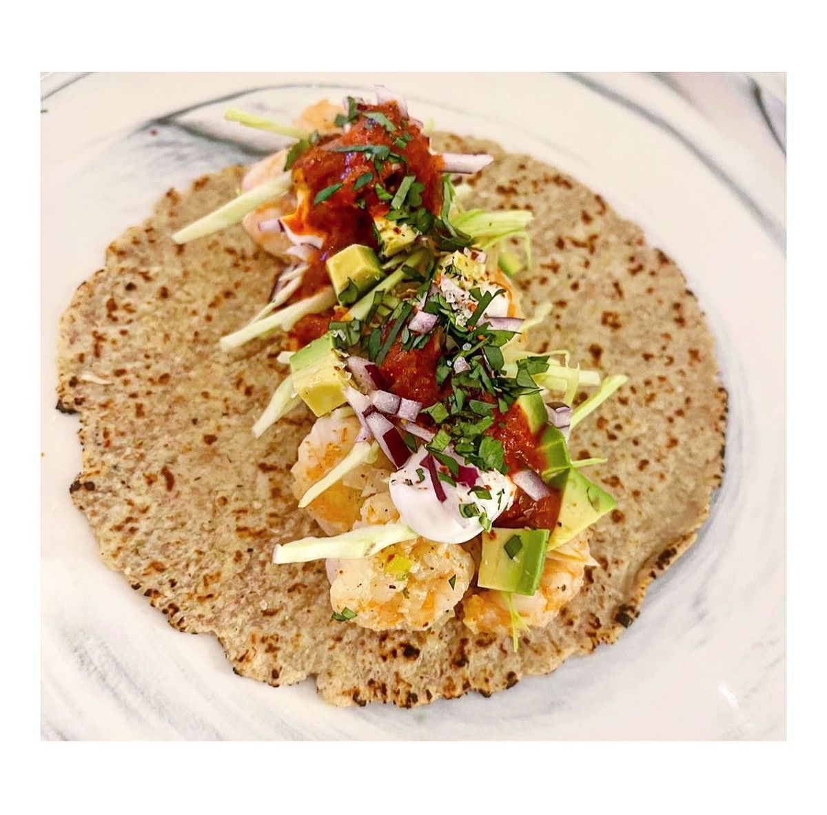 Shrimp wrap open on a tortilla with avocado, cilantro, red onion