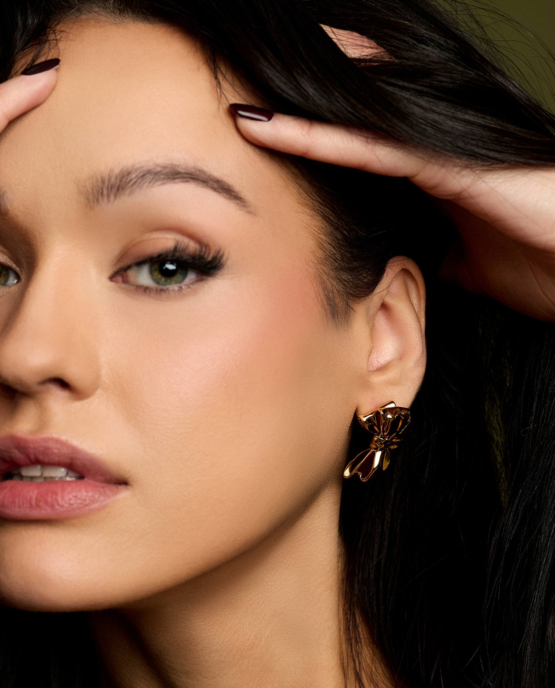 model with her hands in her hair wearing bow earrings - gold