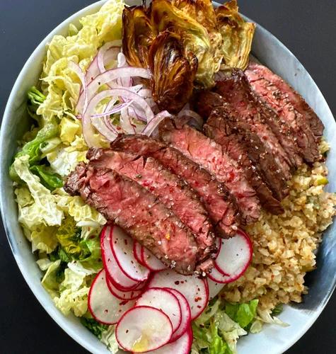 Salad topped with cauliflower rice, roasted artichoke hearts, sliced radish and onion and skirt steak 