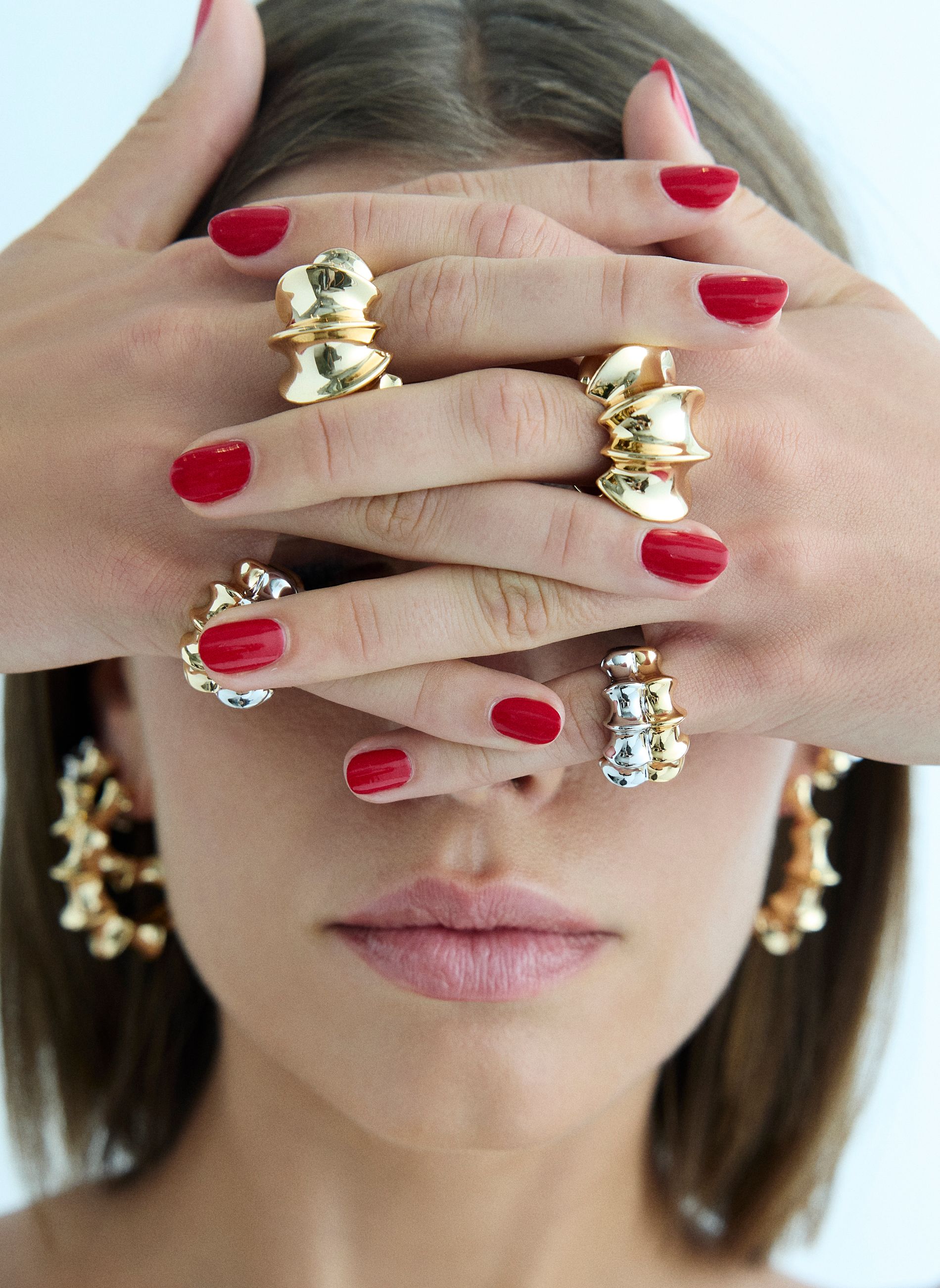 model wearing gold and silver rings with red nails covering her face