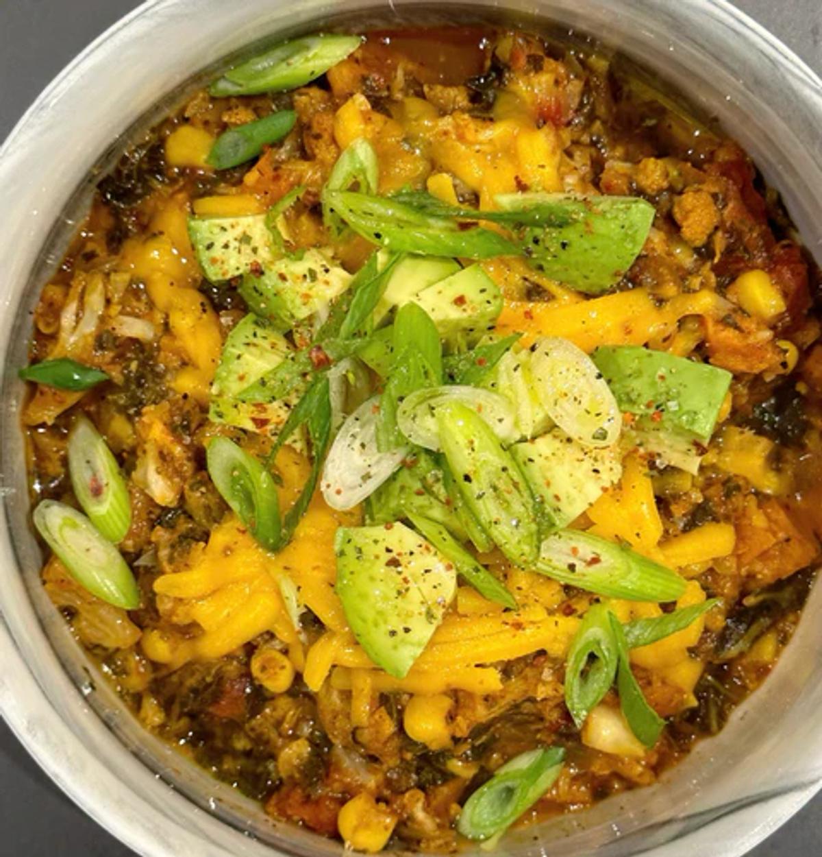 Soup bowl filled with vegan chili packed with veggies and cauliflower "meat" topped with green onion and vegan cheddar cheese. 