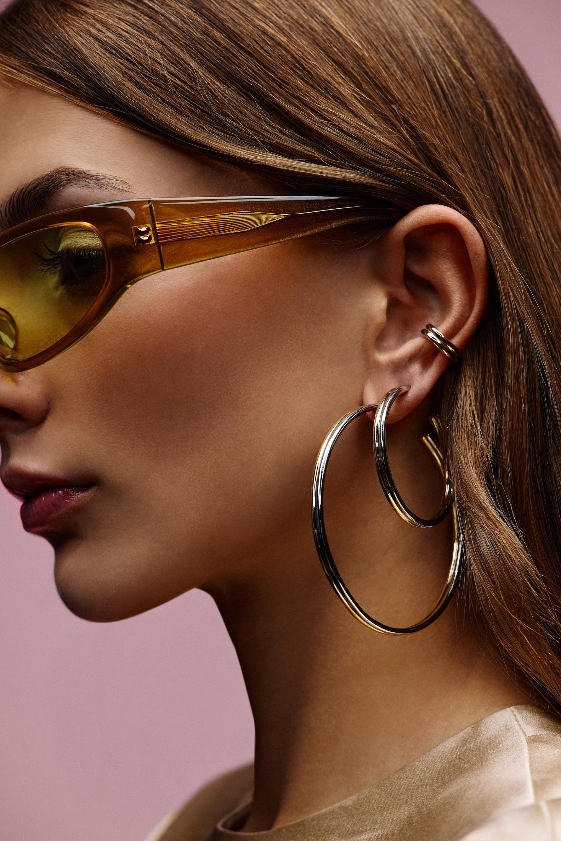 model with glasses eyeshadow and 2 large 2 tone earrings and a 2 tone ear cuff