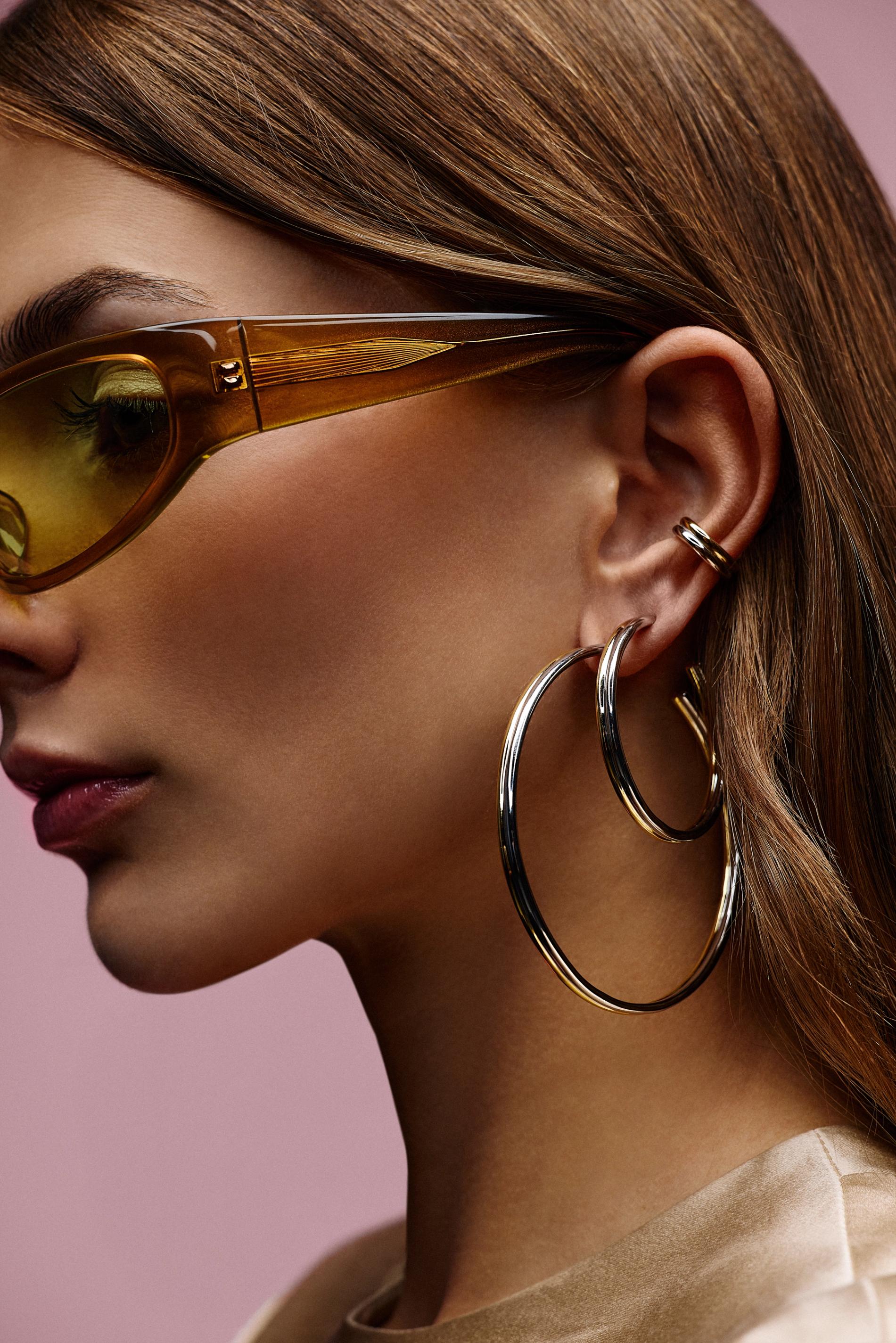 model with glasses eyeshadow and 2 large 2 tone earrings and a 2 tone ear cuff