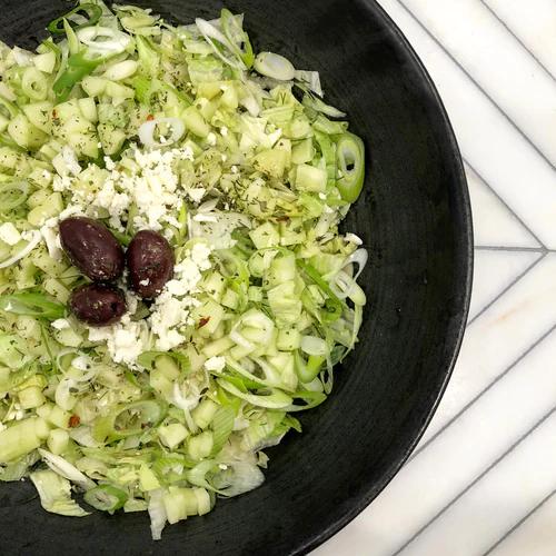 Salad bowl packed with chopped iceberg lettuce, fresh dill, cucumber, feta cheese, green onion, pepperoncinis and kamalata olives.