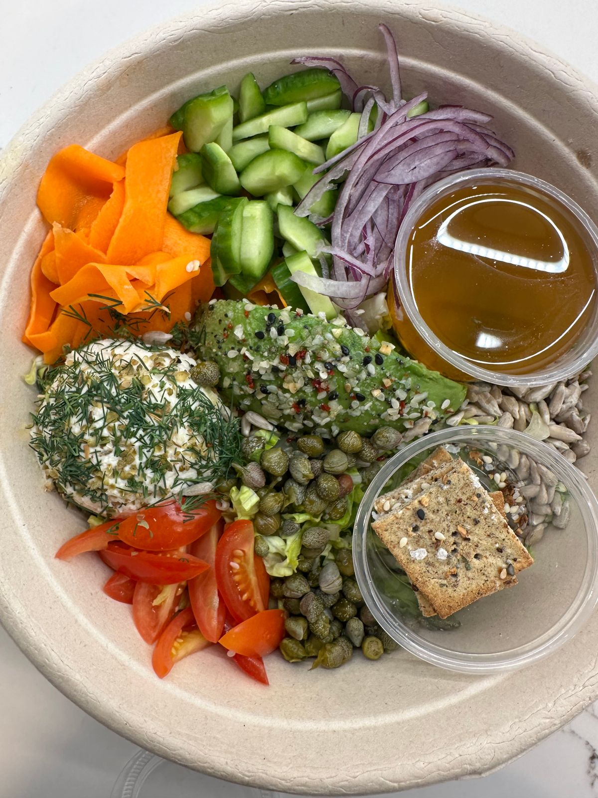 Salad in a bowl with avocado, feta cheese, cucumbers, tomatoes, carrots, onions