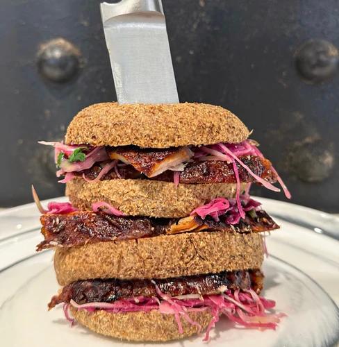 Two grain free buns filled with pork loin roast and crunchy slaw with a knife through the middle.