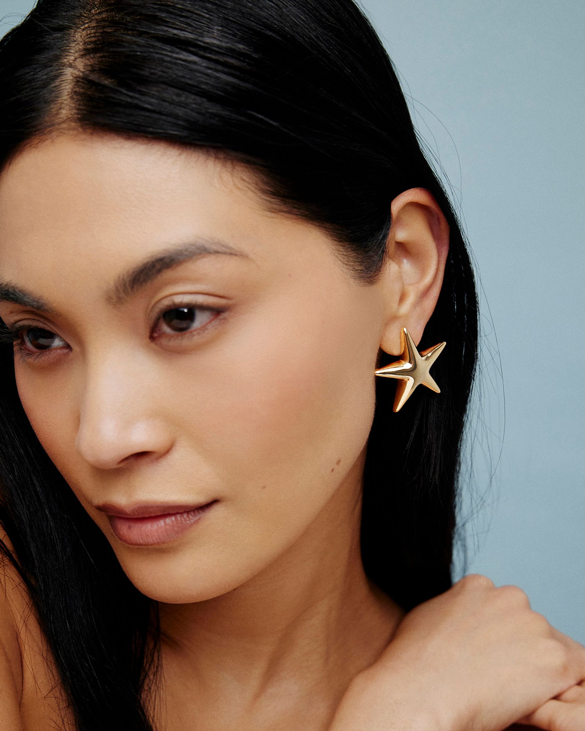 Model in lightweight gold star earrings on a blue background