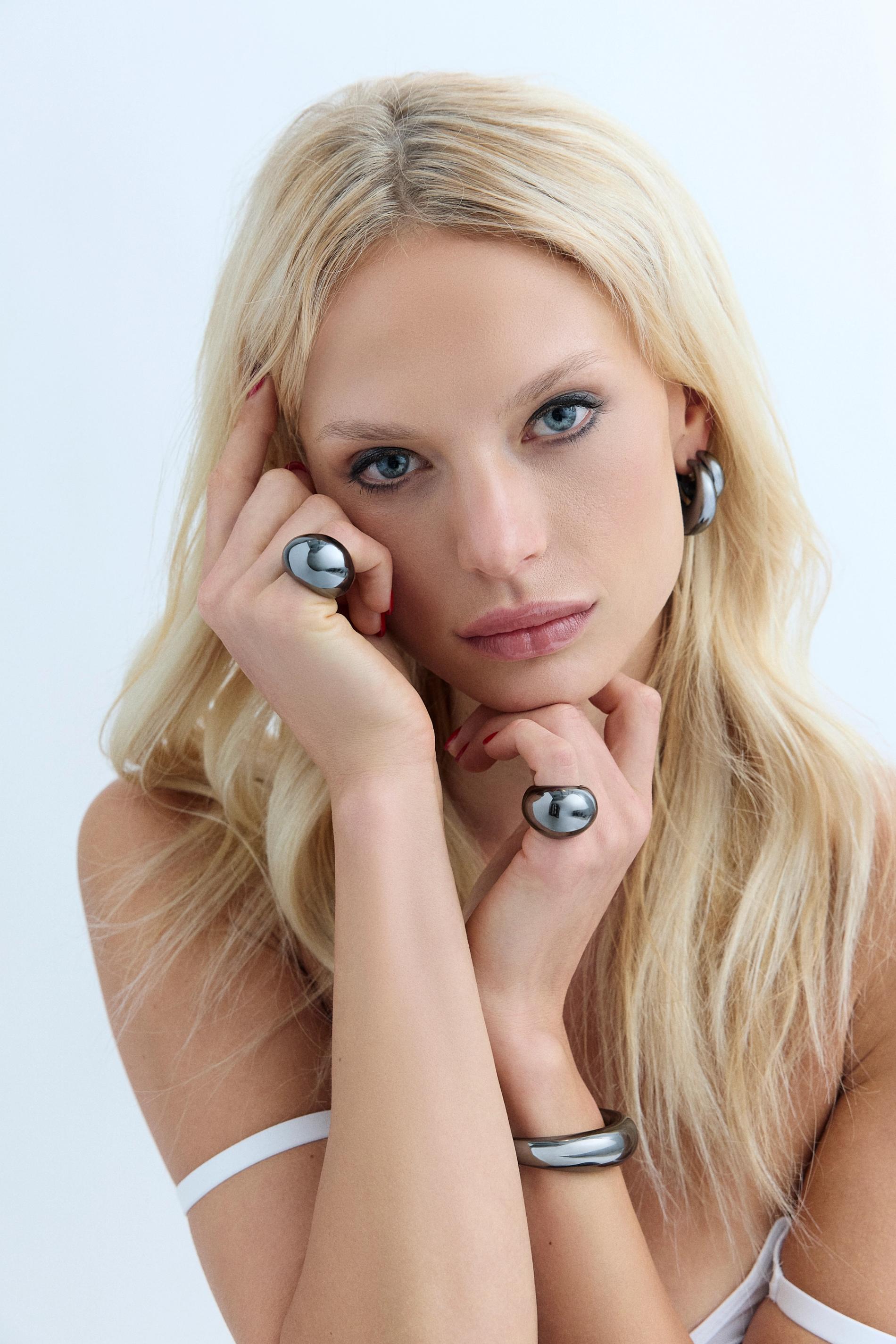 blonde model looking into camera with black hemitite jewelry on, rings, cuffs, and earrings