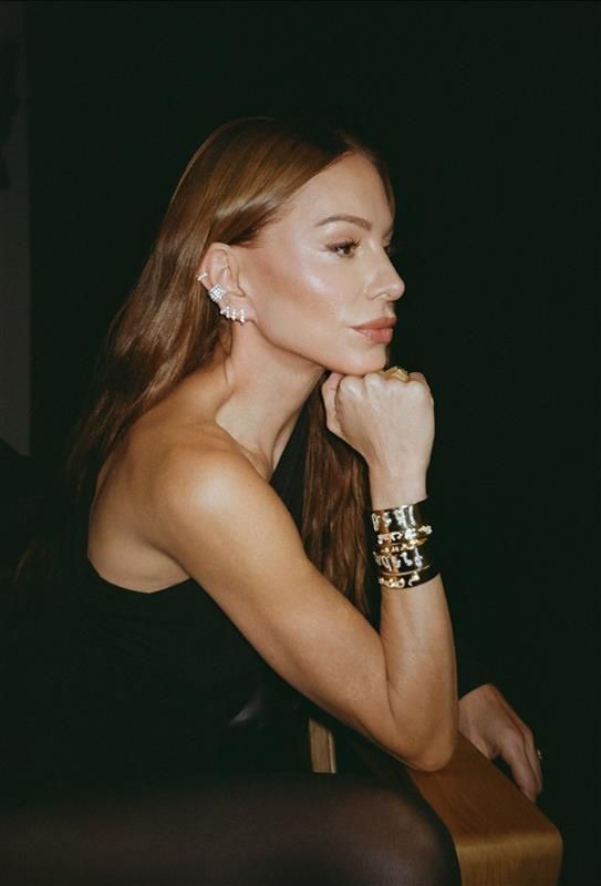 image of jennifer fisher wearing gold bracelets and diamond earrings in a dark room