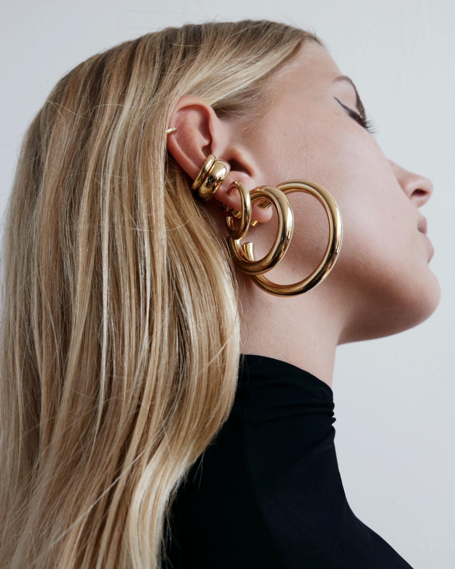 Model wearing multiple gold hoops stacked up her ear looking away from camera