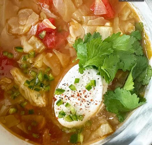 Bowl of warm cabbage soup topped with a dollop of plain coconut yogurt, cilantro, jalapeño and fresh lime.