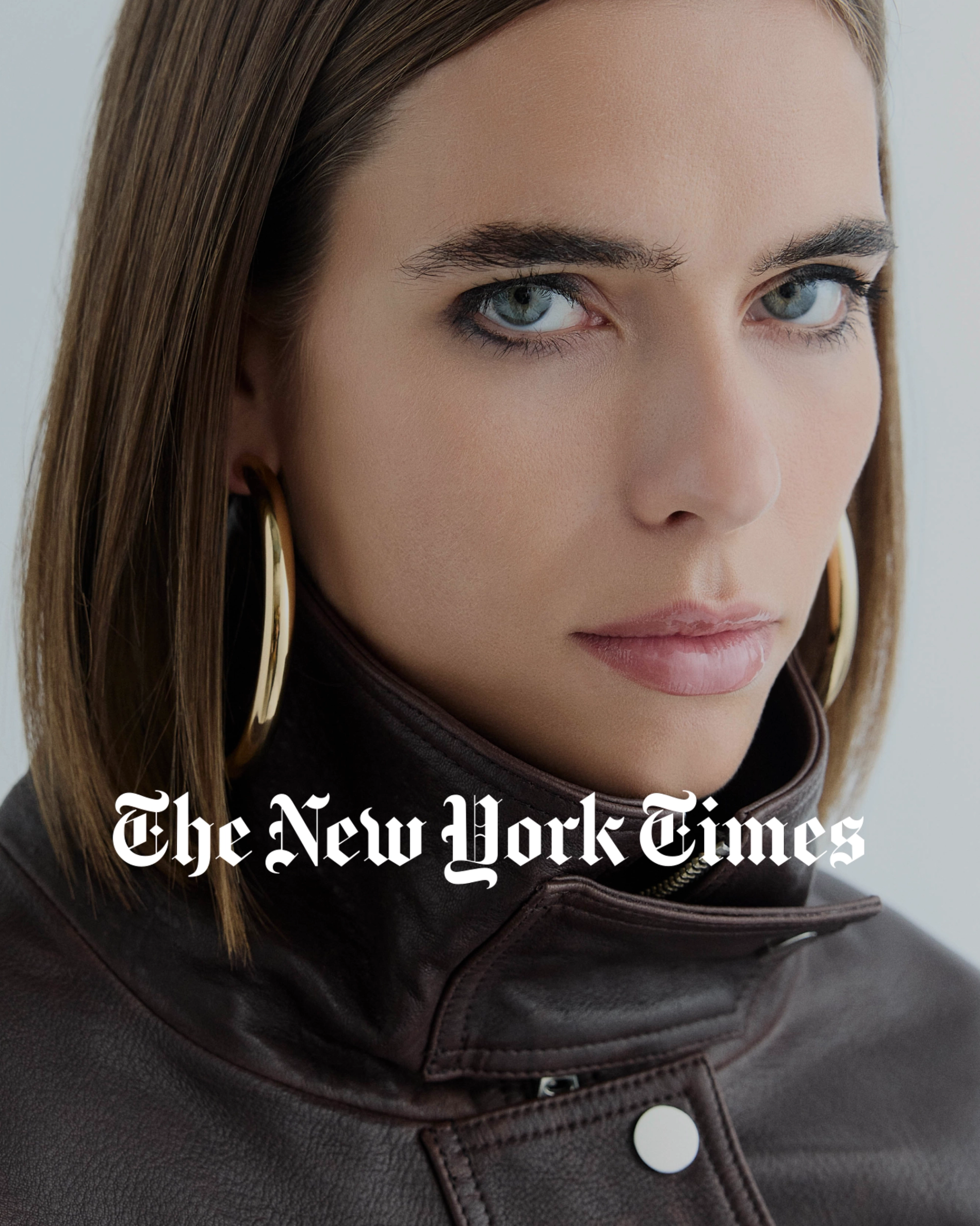 Model looking into camera wearing a brown jacket and gold big hoops