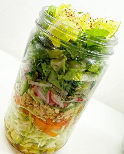 Salad packed with mixed greens, avocado, radish, carrots, tuna, and cucumber in a mason jar. Topped with lime wedges. Perfect for meal prep!