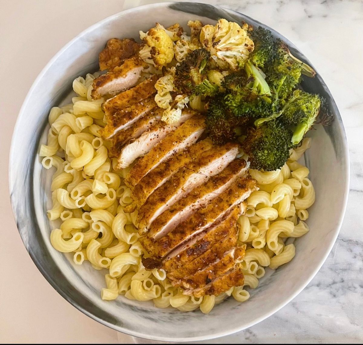 Close up image showing chicken on top of pasta with broccoli on the side