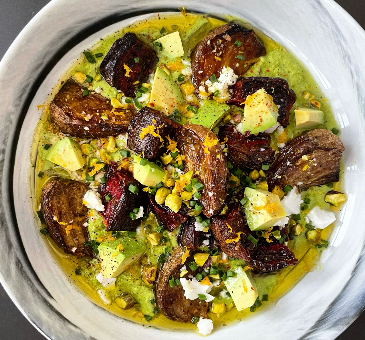 roasted beets in a bowl with green sauce and topped with avocado 