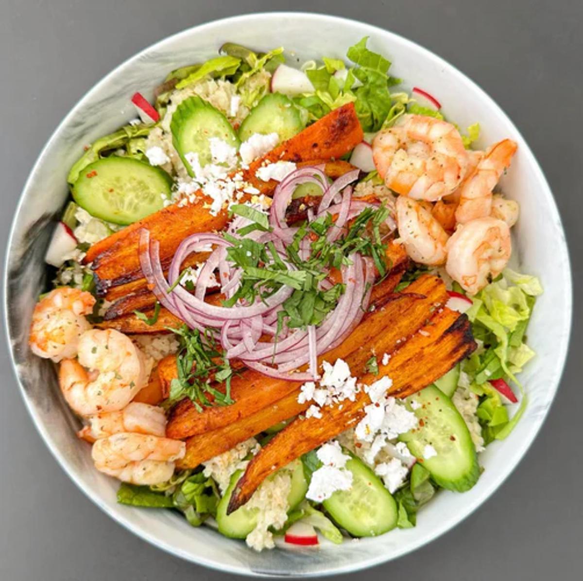 Salad bowl packed with greens, cauliflower rice, shrimp, vegan feta and veggies. 