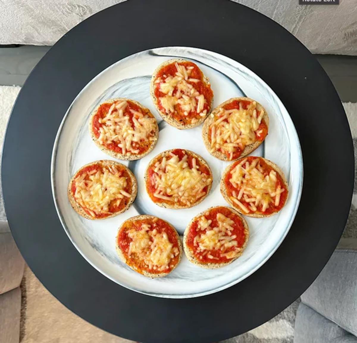 Plate of mini sized snack pizzas topped with tomato sauce and vegan mozzarella cheese