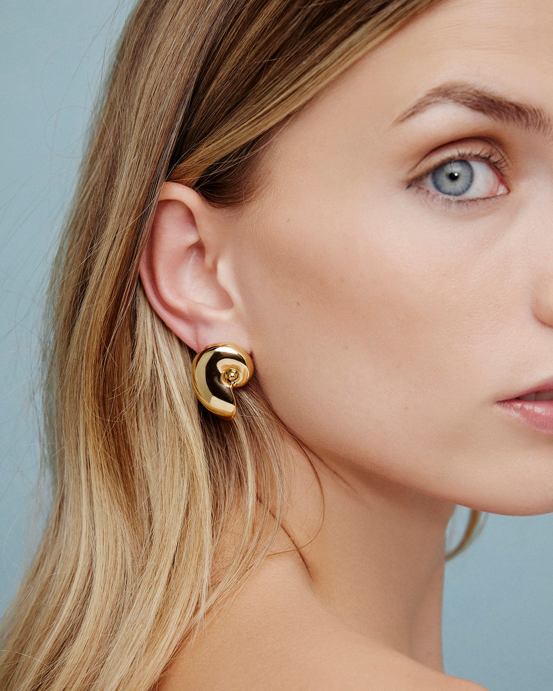 Model in lightweight gold shell earrings on a blue background