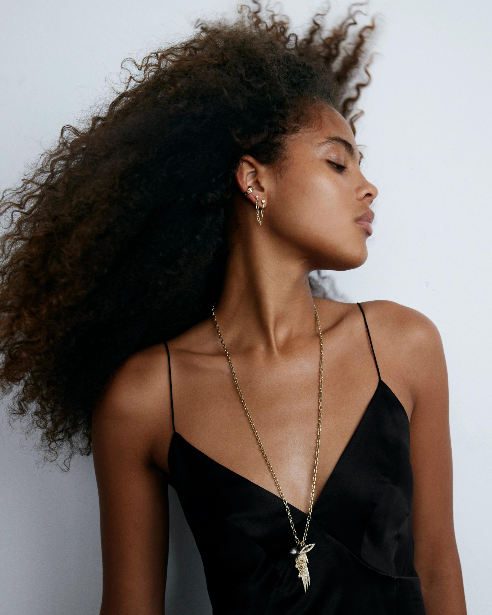 Model with natural hair wearing long chain with assorted charms over black camisole.