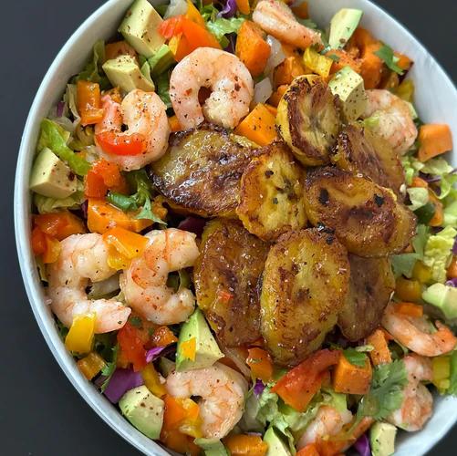 Salad bowl filled with greens, avocado, red, yellow, and orange peppers, shrimp and pan fried plantains.