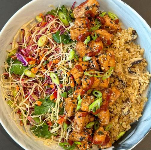 Bowl with shiitake cauliflower rice base topped with chunks of salmon and a crunchy cabbage slaw.