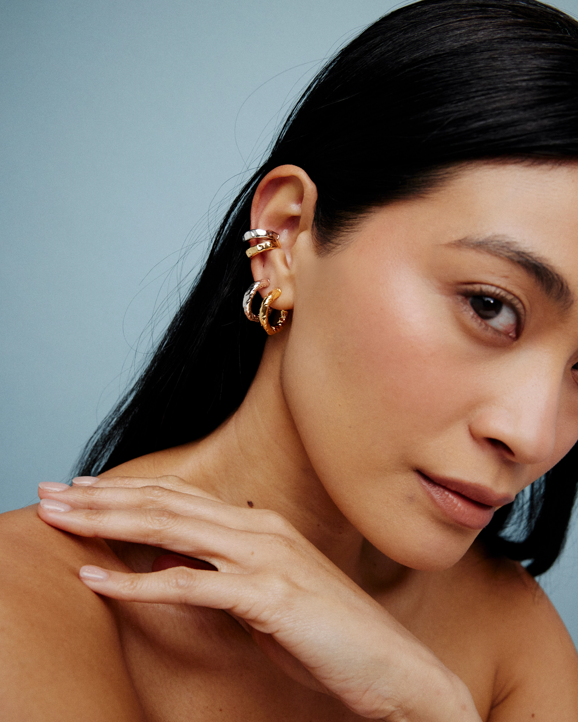 Model wearing gold hoops, diamond studs, and a gold cuff.