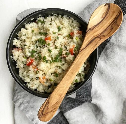 Bowl filled with cauliflower rice topped with chopped green onions and red bell pepper. Sprinkled with JF Universal Salt.
