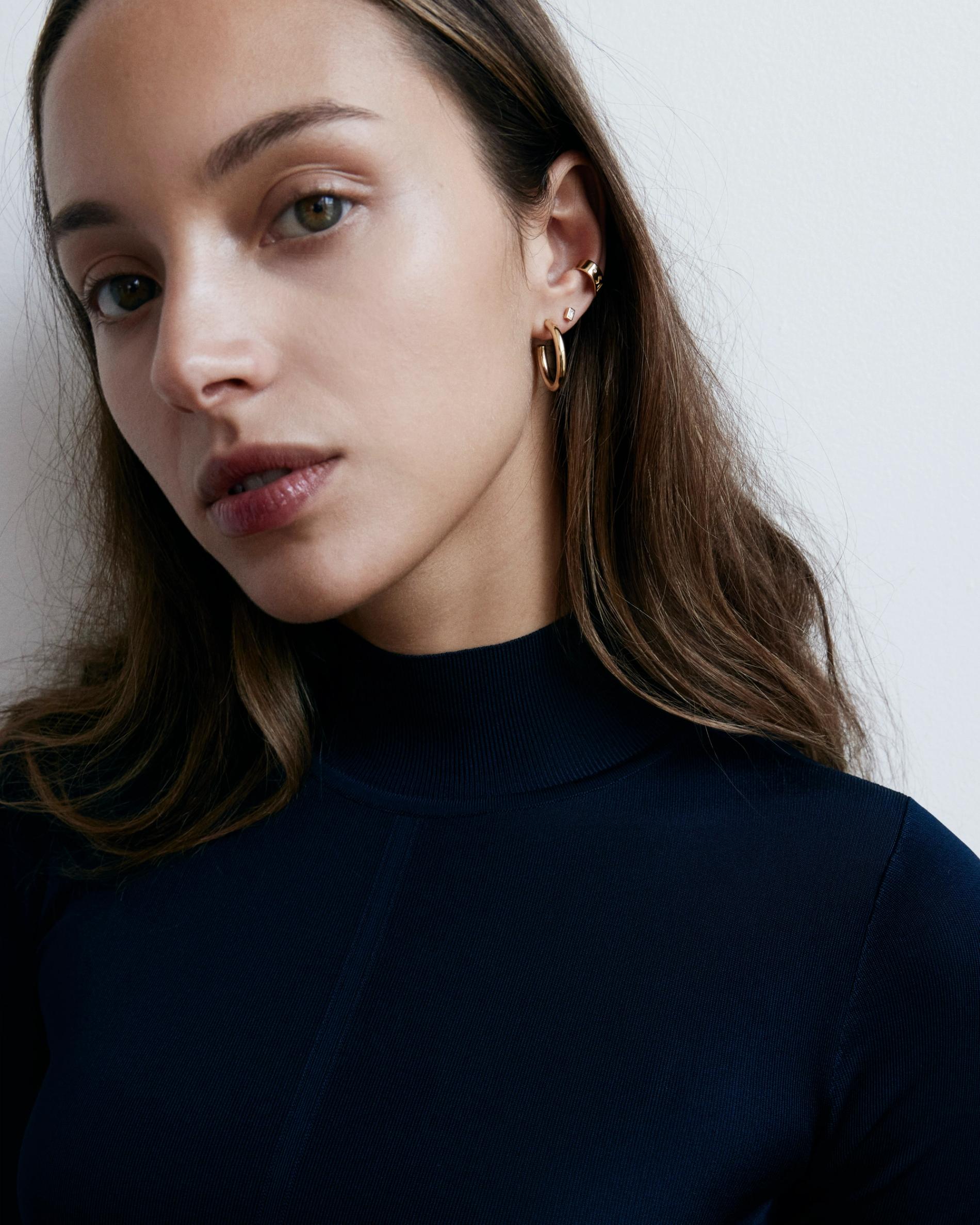Model wearing high collar turtleneck and diamond earrings.