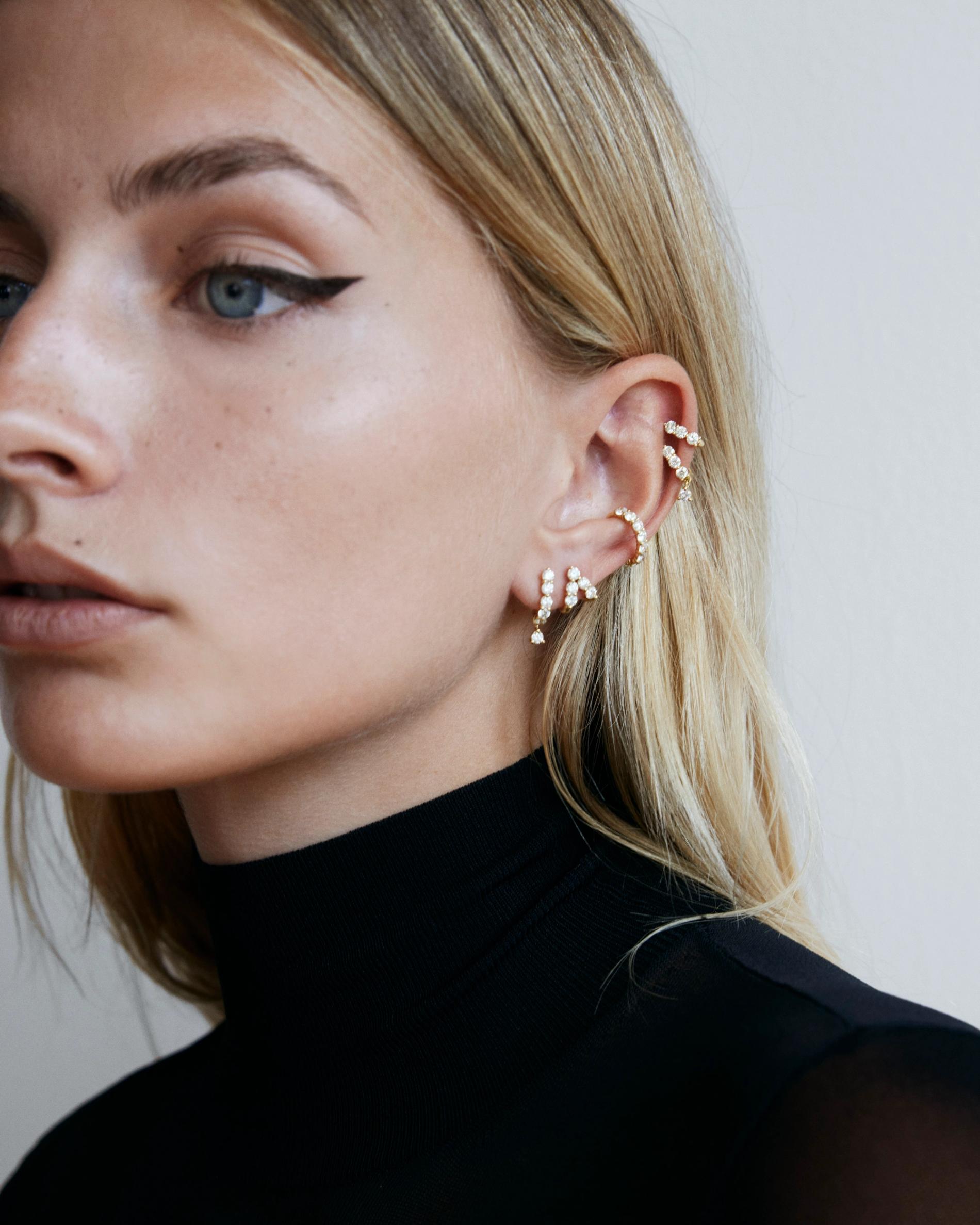 Close up of model looking past camera wearing multiple diamond earrings and earring Huggies on a single ear.
