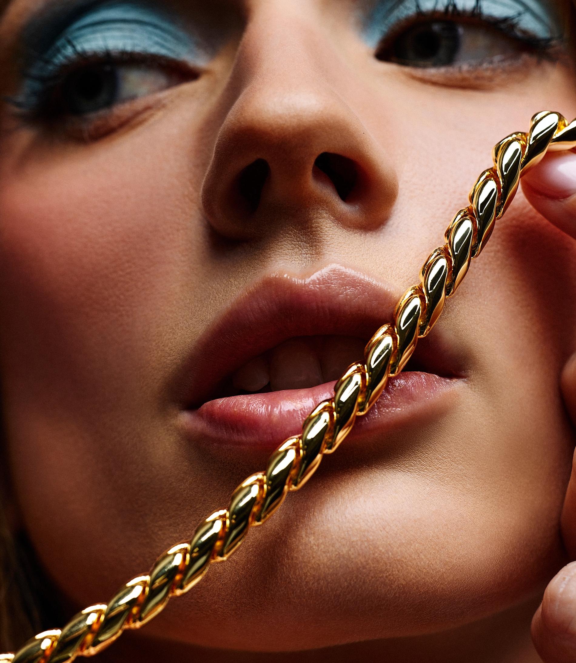 model with blue eyeshadow holding a gold chain in front of her face