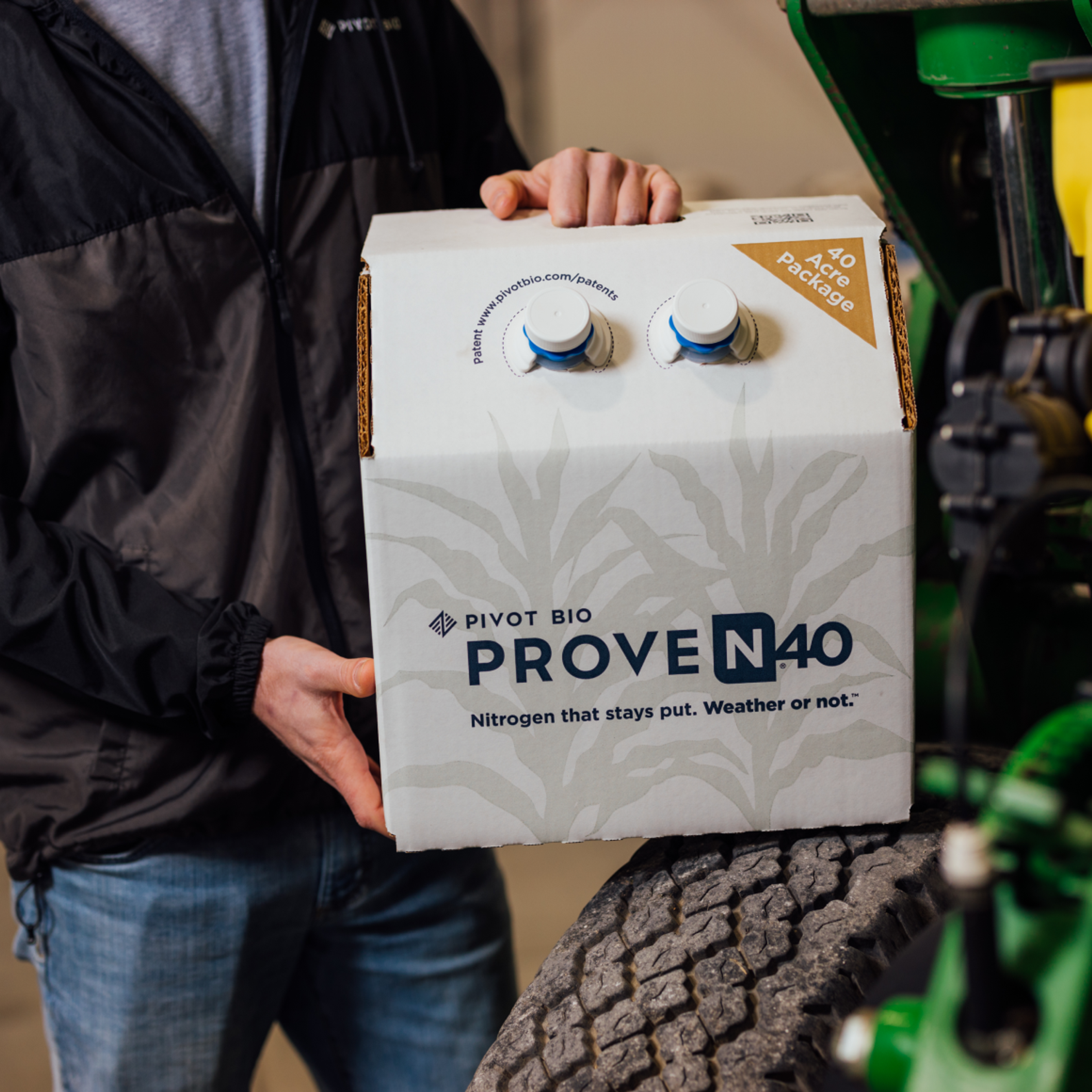 Image of a farmer holding a box of Pivot Bio product on a tractor tire