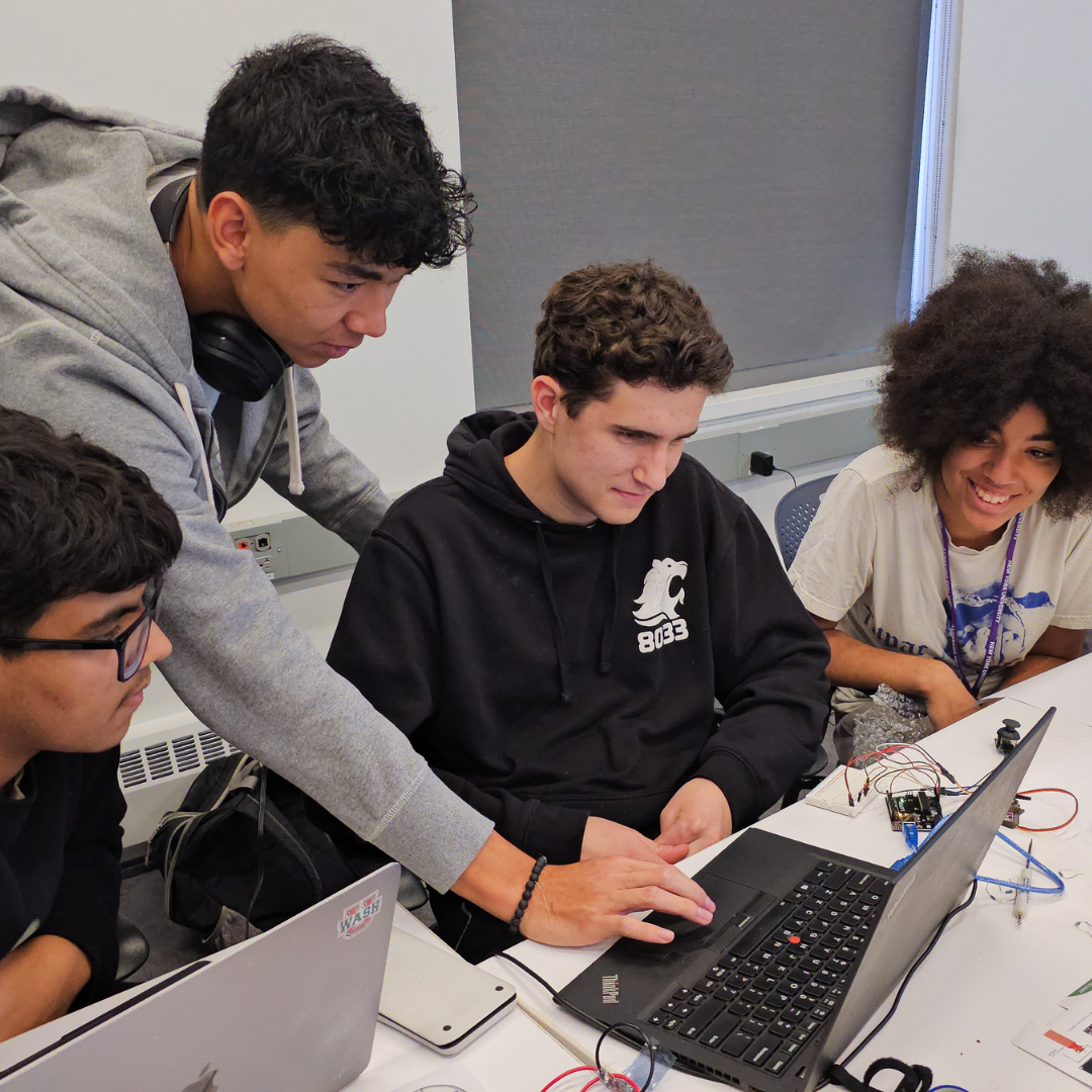 SPARC program students at NYU Tandon working together on a coding and robotics project, with one student pointing at a laptop screen while others engage in discussion