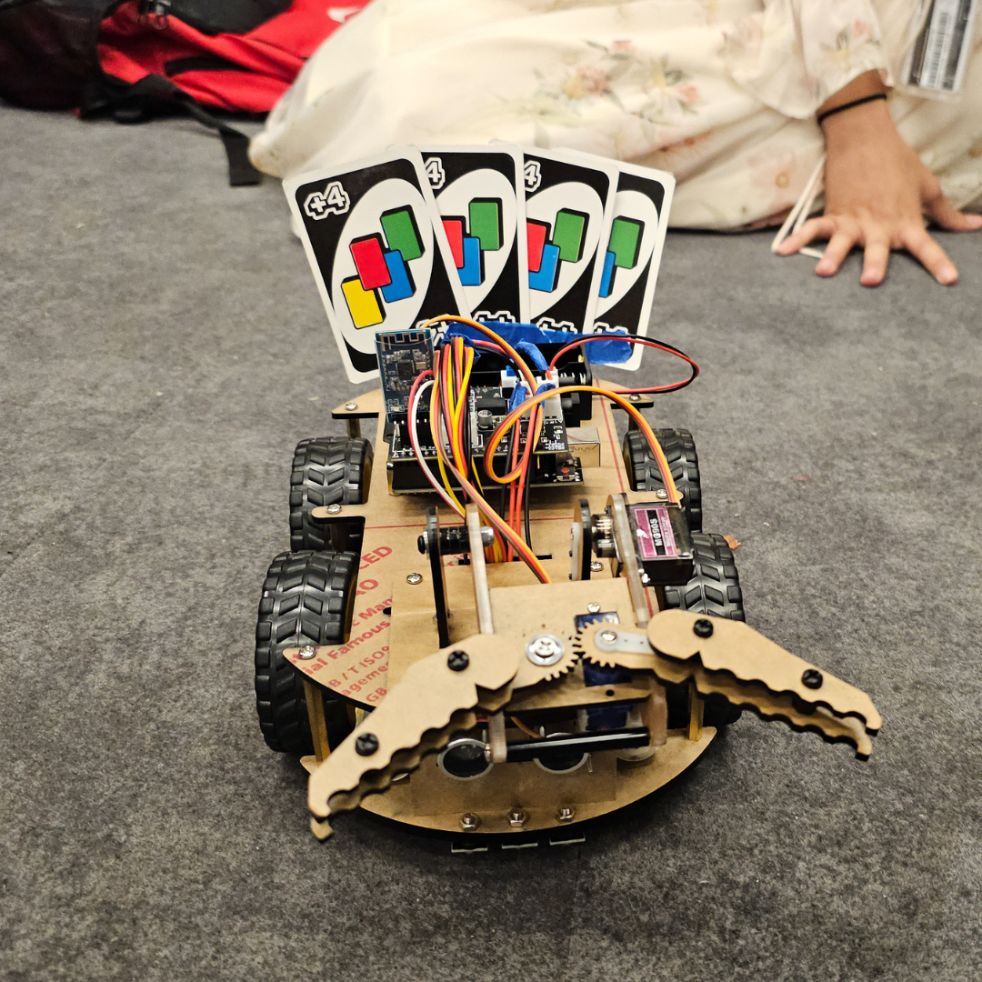 A student-designed robotic vehicle with mechanical claws holding UNO cards, created for a STEM project at NYU Tandon.