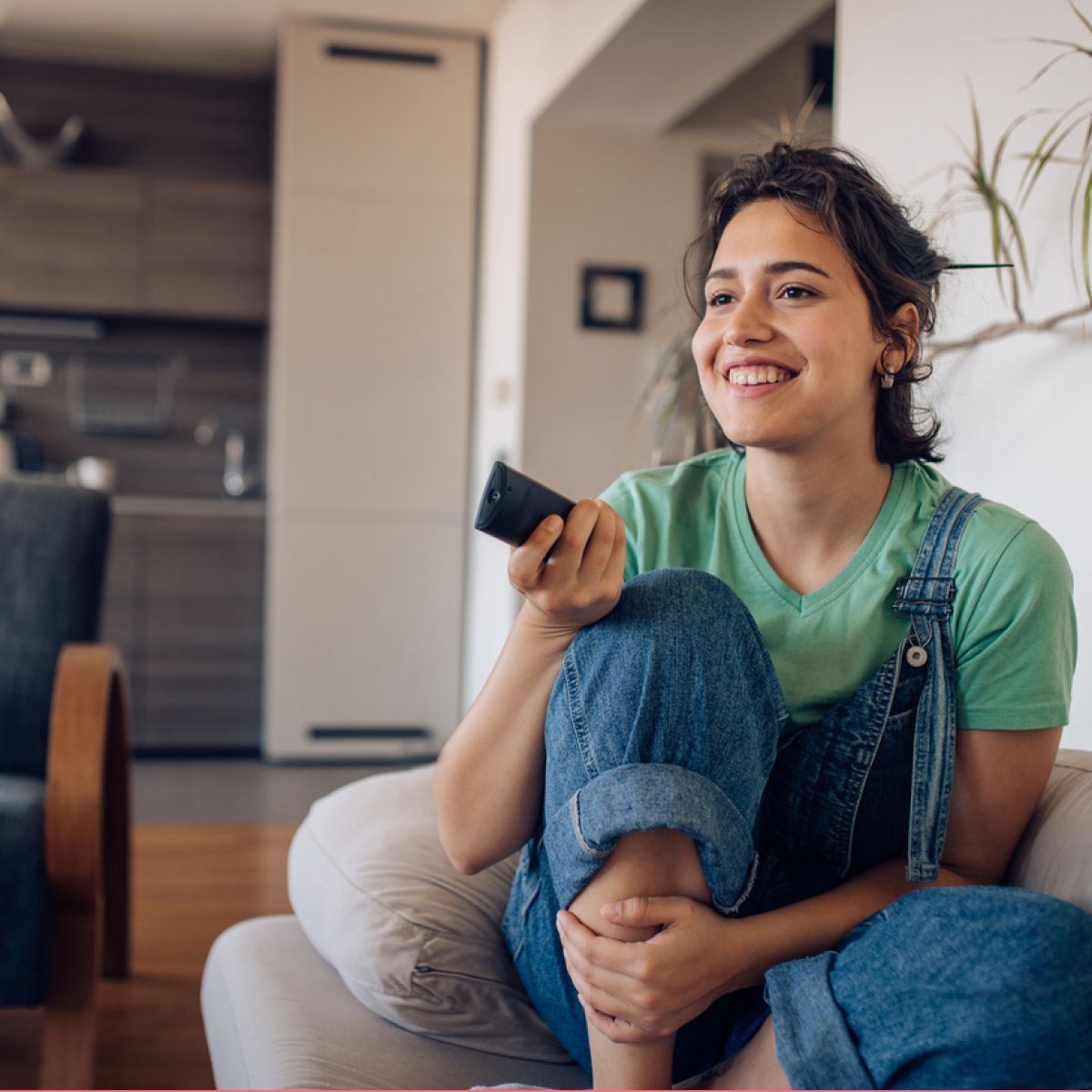 Woman smiling watching TV on couch with remote
