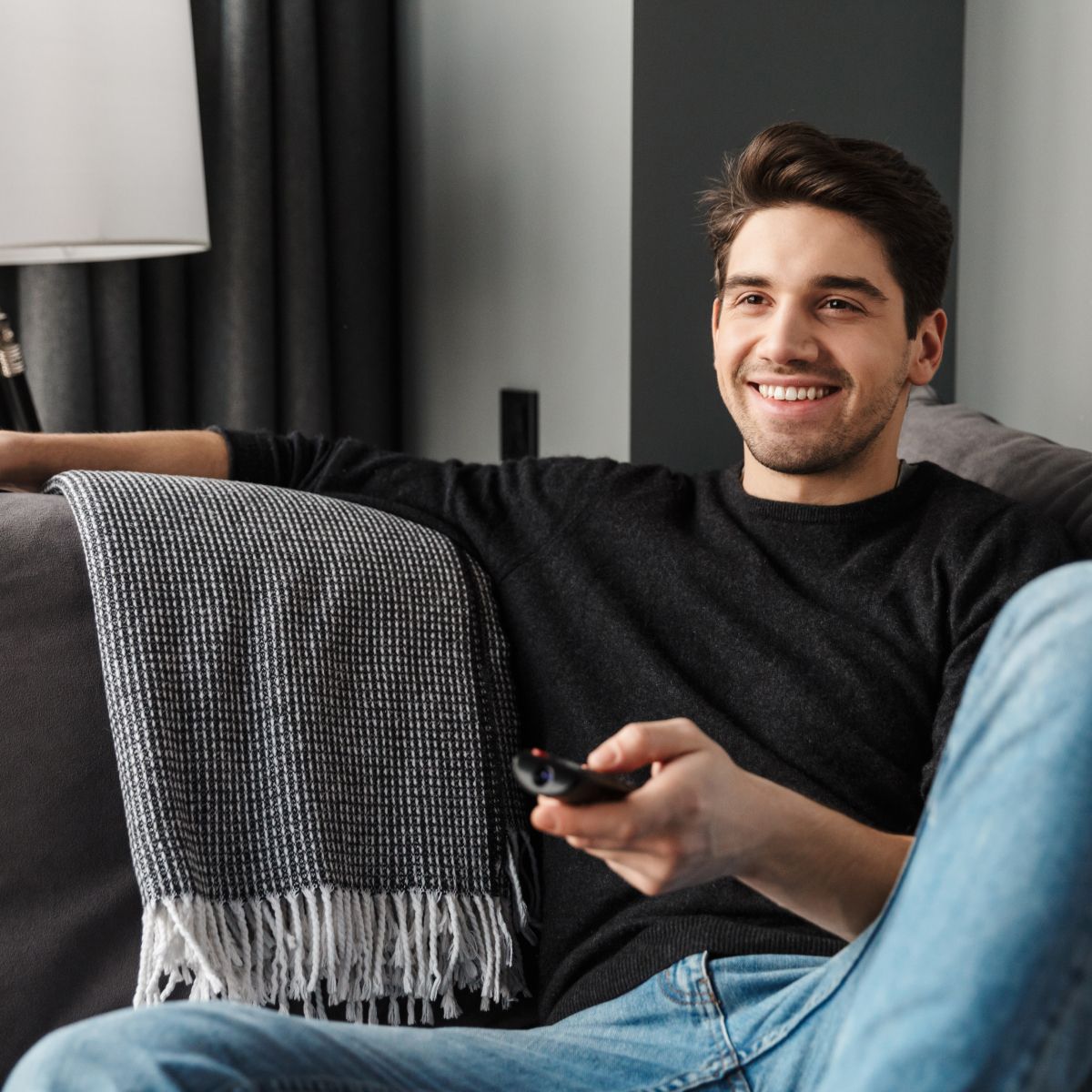 Man smiling watching TV on couch with remote