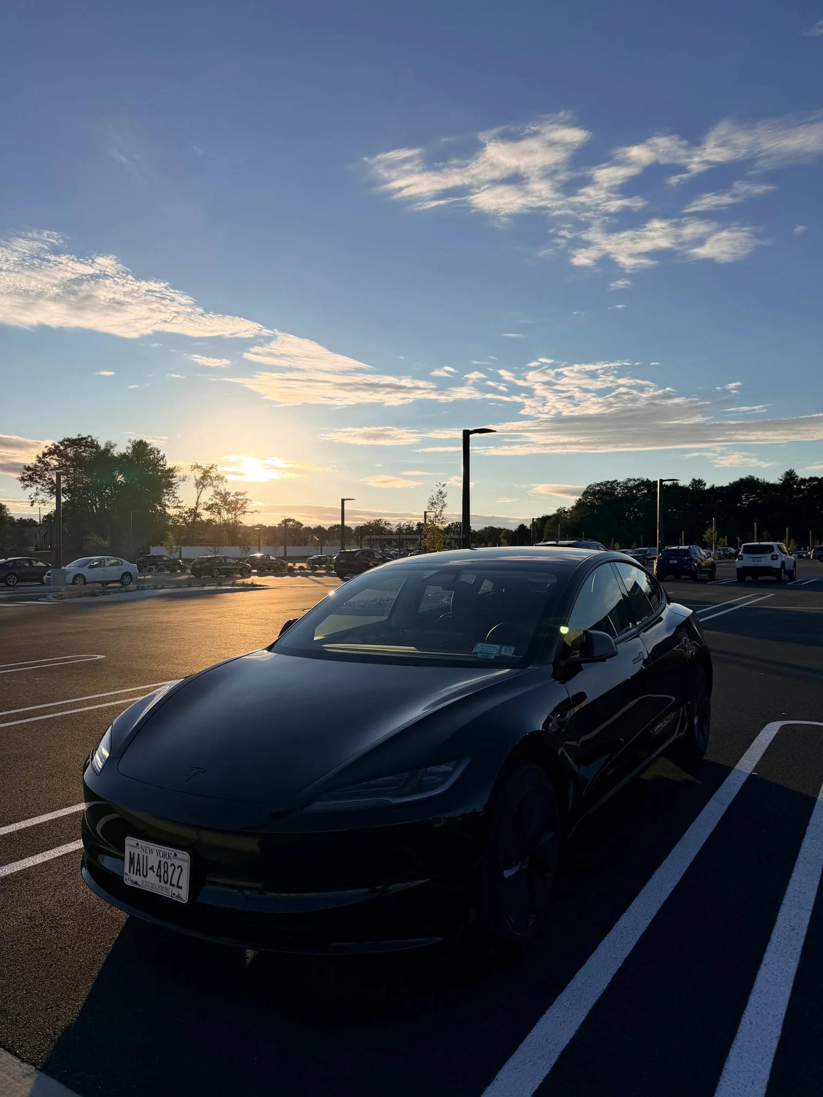 Front three-quarter view of a black Tesla at sunset.