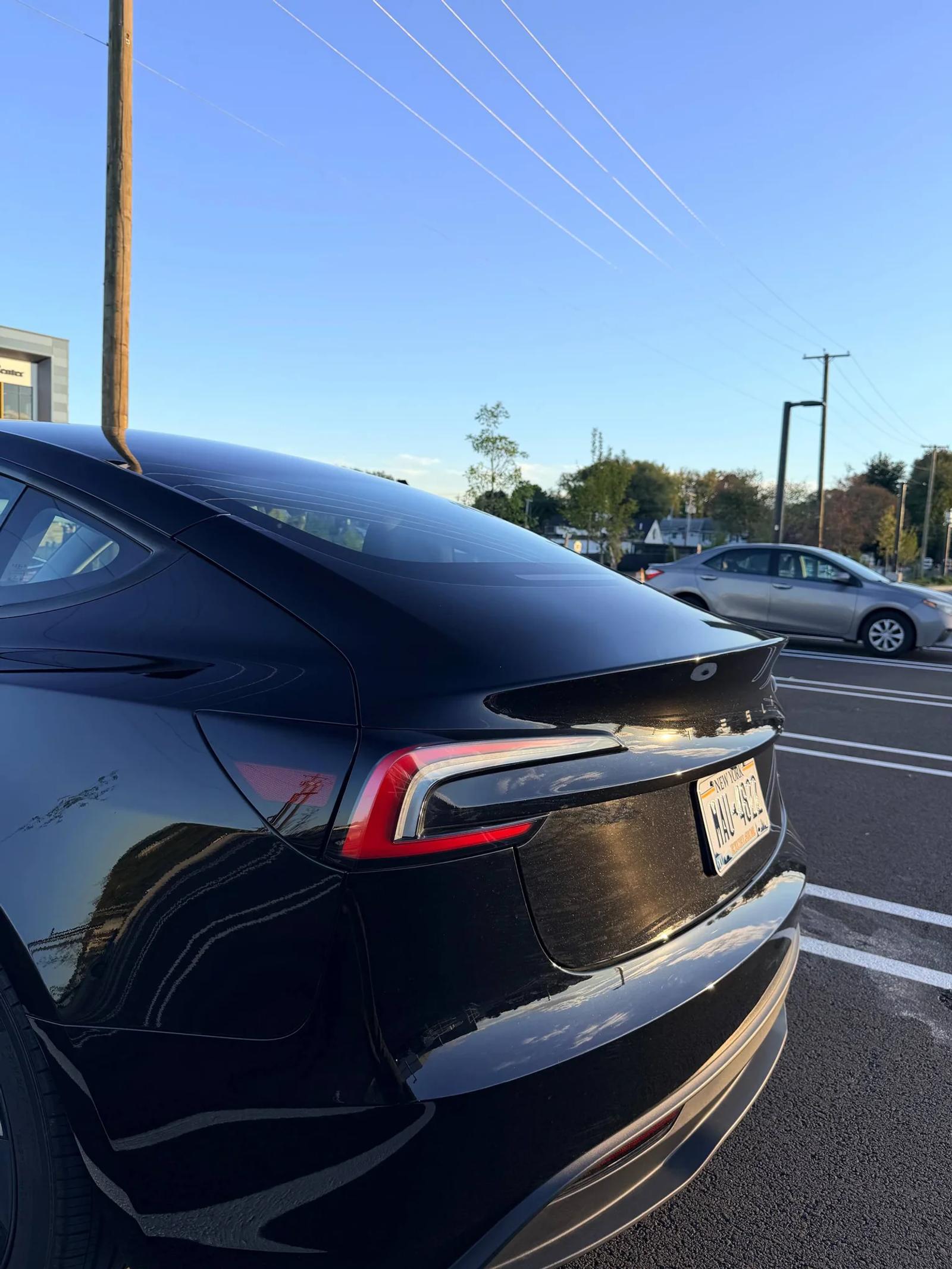 Rear three-quarter view of a black Tesla, showing the rear fender, trunk and taillight.
